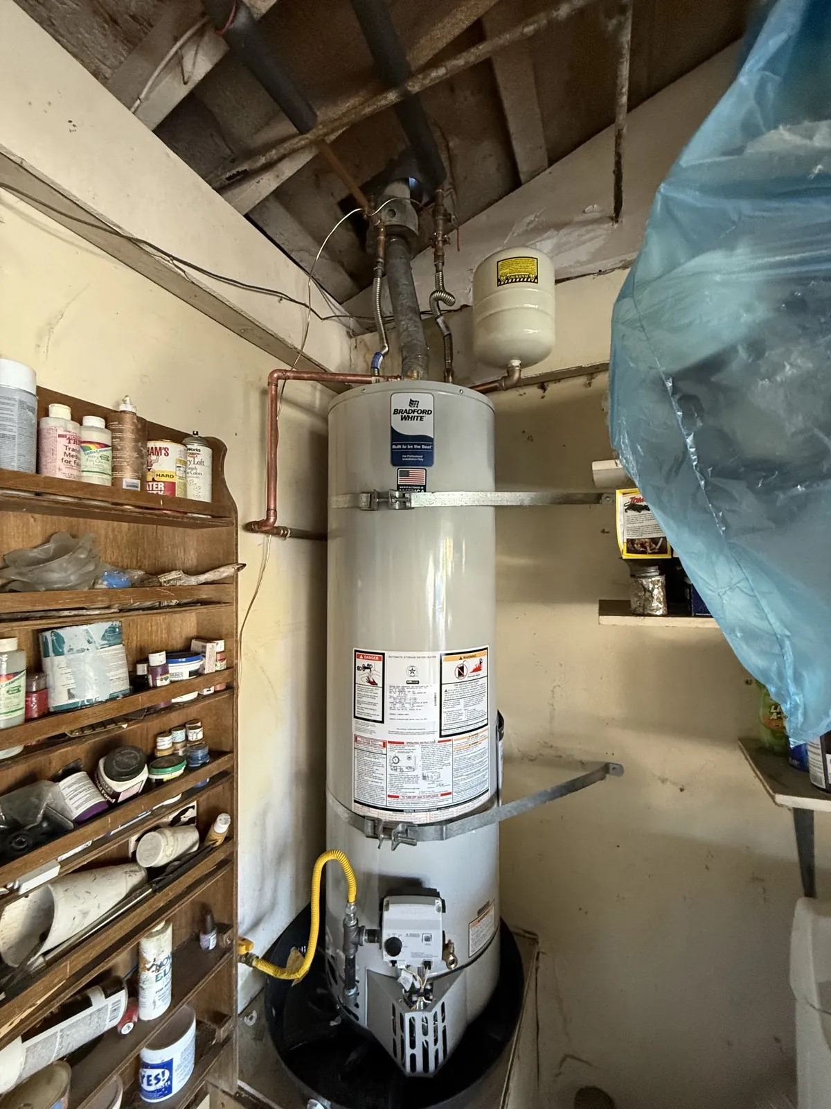 A gas tank water heater in a garage with its expansion tank and seismic strap